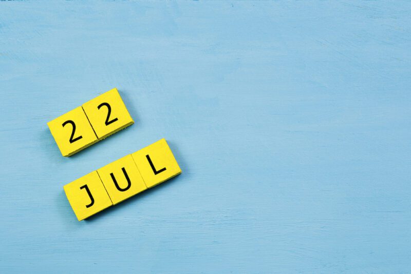 JUL 22, yellow cube calendar on blue wooden surface with copy space